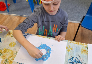 Chłopiec siedzi przy stole i wykonuje pracę plastyczną