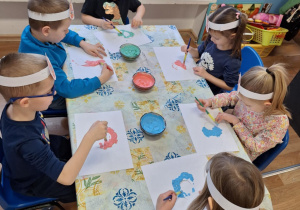 Grupa dzieci siedzi przy stole i wykonuje pracę plastyczną