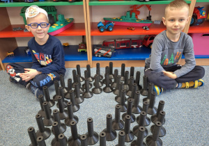 Chłopcysiedzą na dywanie i pokazują pączka zrobionego z klocków