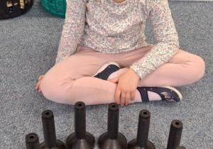 Dziewczynkac siedzi na dywanie i pokazuje pączka zrobionego z klocków