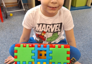 Chłopiec siedzi na dywanie i pokazuje pączka zrobionego z klocków