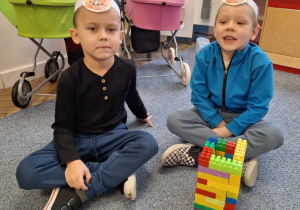 Chłopcy siedzą na dywanie i pokazują pączka zrobionego z klocków