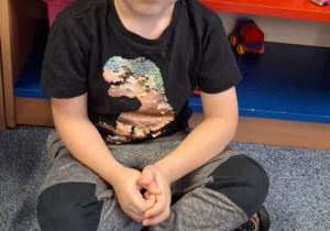 Chłopiec siedzi na dywanie i pokazuje pączka zrobionego z klocków