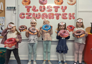 Grupa dziewczynek stoi na dywanie i pozują do zdjęcia z obrazkami pączków