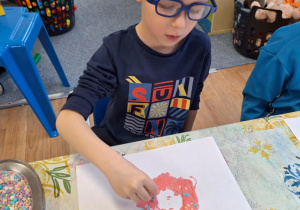 Chłopiec siedzi przy stole i wykonuje pracę plastyczną