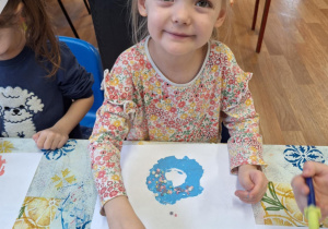 Dziewczynka siedzi przy stole i wykonuje pracę plastyczną