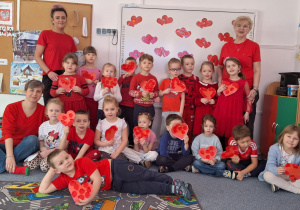 Cała grupa stoi i pozują do zdjęcia z sercami zrobinymi przez siebie