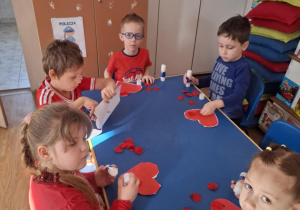 Grupa dzieci wykonuje pracę plastyczną przy stoliku