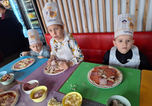 Grupa dzieci siedzi przy stole i robią swoją pizze