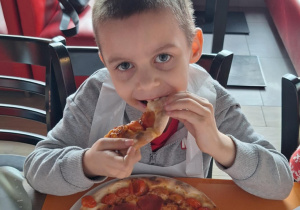 Chłopiec je pizzę przez siebie zrobioną