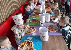 Grupa dzieci siedzi przy stole i je pizzę