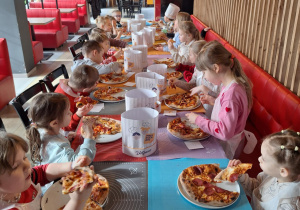 Grupa dzieci siedzi przy stole i je pizzę