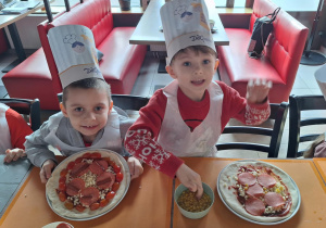 Chłopcy siedzą przy stole i robią swoje pizze