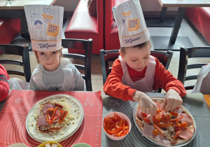 Dwoje dzieci siedzi przy stole i robi swoje pizze