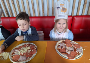 Dwoje dzieci siedzi przy stole i robi swoje pizze