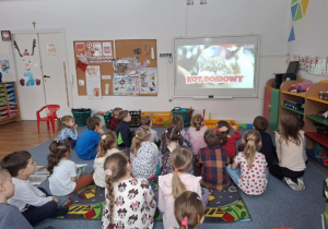 Dzieci siedzą na dywanie i oglądają film edukacyjny-koty domowe