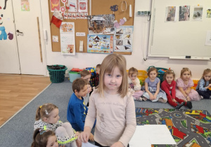 Dziewczynka stoi na dywanie i pokazuje obrazek z kotem z bajki