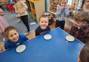 Grupa dzieci siedzi przy stoliku i będzie piła mleko z talerzyka jak kot