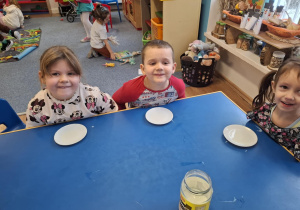 Grupa dzieci siedzi przy stoliku i będzie piła mleko z talerzyka jak kot