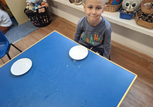 Chłopiec siedzi przy stoliku i będzie pił mleko z talerzyka jak kot