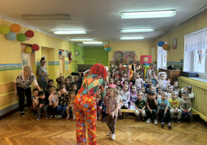 Grupa dzieci i dwie panie oglądają pokaz w wykonaniu pani w kolorowym stroju