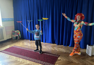 Pani w kolorowym stroju i chłopiec z czterema kręcącymi krążkami na kijach