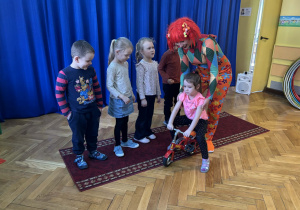 Dzieci patrzą jak pani prowadzi dziecko na minimalistycznym rowerku