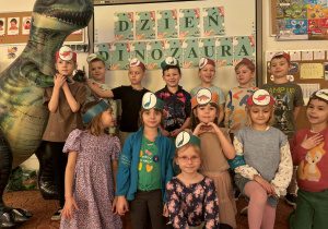 Grupa dzieci z dinozaurem przed napisem Dzień Dinozaua