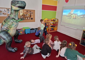 Dzieci oglądają prezentację o dinozaurach na tablicy interaktywnej