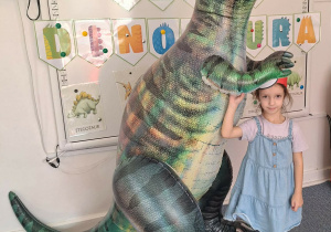 Dziewczynka pozuje do zdjęcia z dmuchanym dinozaurem
