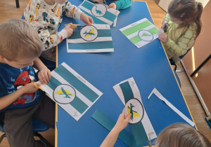 Grupa dzieci siedzi przy stoliku wycina opaski na głowę