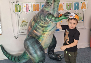 Chłopiec pozuje do zdjęcia z dmuchanym dinozaurem