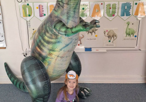 Dziewczynka pozuje do zdjęcia z dmuchanym dinozaurem