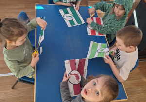 Grupa dzieci siedzi przy stoliku wycina opaski na głowę