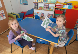 Grupa dzieci siedzi przy stoliku i wypycha z kartonu postać dinozaura