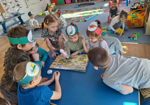 Grupa dzieci siedzi przy stoliku i ogląda książkę o dinozaurach