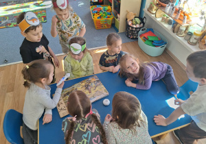 Grupa dzieci siedzi przy stoliku i ogląda książkę o dinozaurach