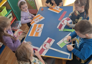 Grupa dzieci siedzi przy stoliku wycina opaski na głowę