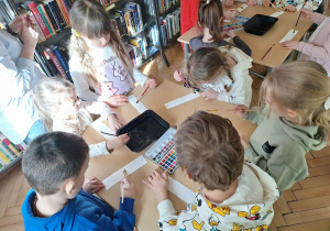 Grupa dzieci siedzi przy stoliku i wykonuje zakładkę do książki