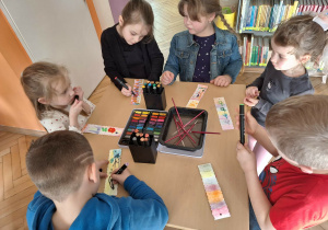 Grupa dzieci siedzi przy stoliku i wykonuje zakładkę do książki