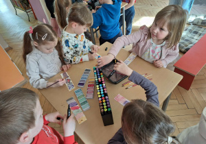 Grupa dzieci siedzi przy stoliku i wykonuje zakładkę do książki