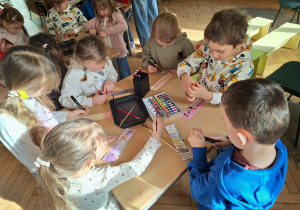 Grupa dzieci siedzi przy stoliku i wykonuje zakładkę do książki