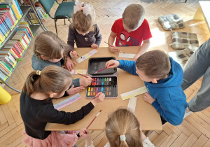 Grupa dzieci siedzi przy stoliku i wykonuje zakładkę do książki