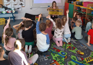 Dzieci siedzą na dywanie i słuchają pani prowadzącej warsztaty