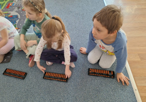 Grupa dzieci siedzi na dywanie i ćwiczy na własnym liczydle