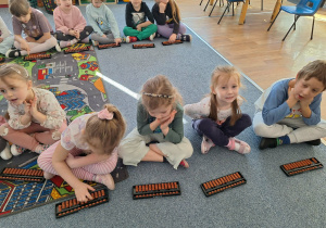 Grupa dzieci siedzi na dywanie i ćwiczy na własnym liczydle