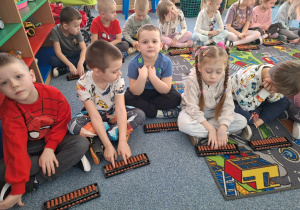 Grupa dzieci siedzi na dywanie i ćwiczy na własnym liczydle