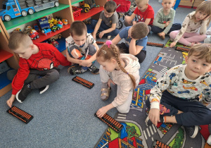 Grupa dzieci siedzi na dywanie i ćwiczy na własnym liczydle