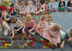 Grupa dzieci siedzi na dywanie i ćwiczy na własnym liczydle