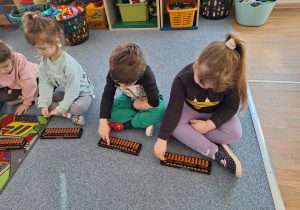 Grupa dzieci siedzi na dywanie i ćwiczy na własnym liczydle